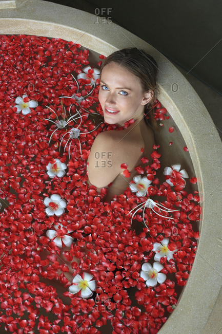 Woman sitting in spa bath filled with red and white flowers