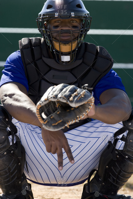 Baseball catcher crouching on pitch, making secret signal with fingers, front view, portrait