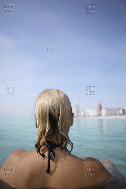 Woman relaxing in sea, looking at view into land, rear view