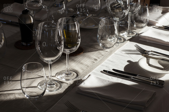 Empty wine and water glasses around place setting at dinner table with strong light