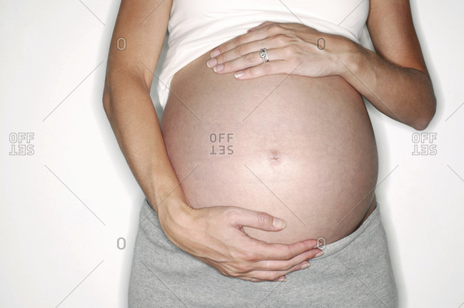 Pregnant woman holding her exposed swollen abdomen. She is in her third trimester.