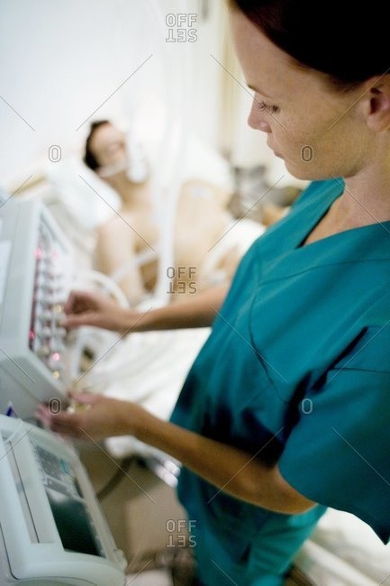 Nurse adjusting controls on a ventilator attached to an unconscious patient