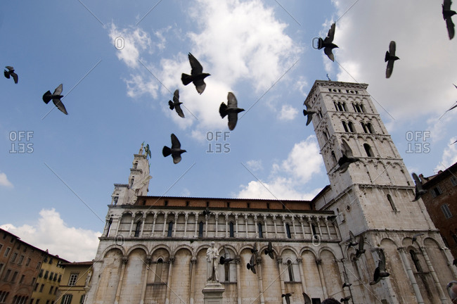 Birds fly across a cloudy sky in San Michele in Foro Basilica in Lucca, Tuscany