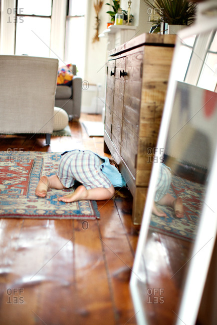Little boy searching something under sideboard in living room