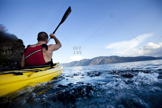 Young man paddles yellow kayak on lake