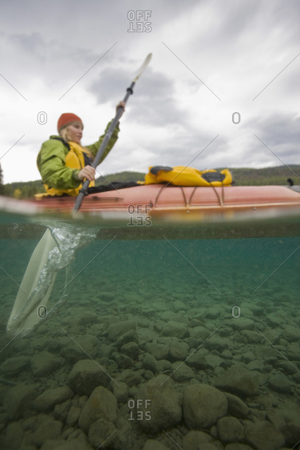 Woman sea kayaking on a lake as seen from below deep in Glacier National Park