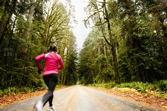 A female jogging down a road next to tall trees covered in moss