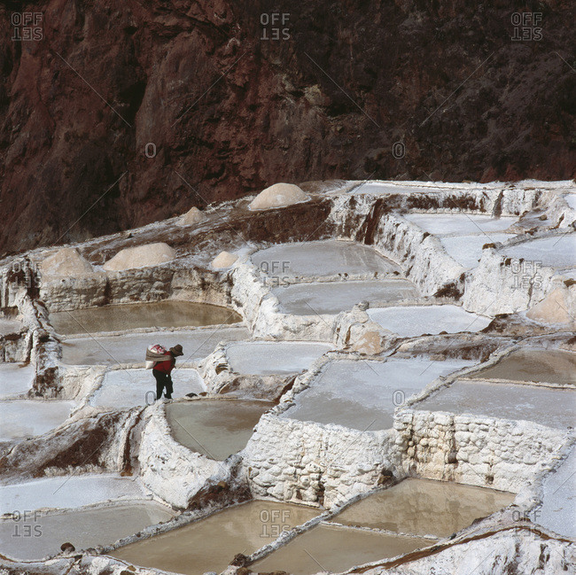 Person standing on terraced salt ponds on a mountainside,Inca Trail, Peru