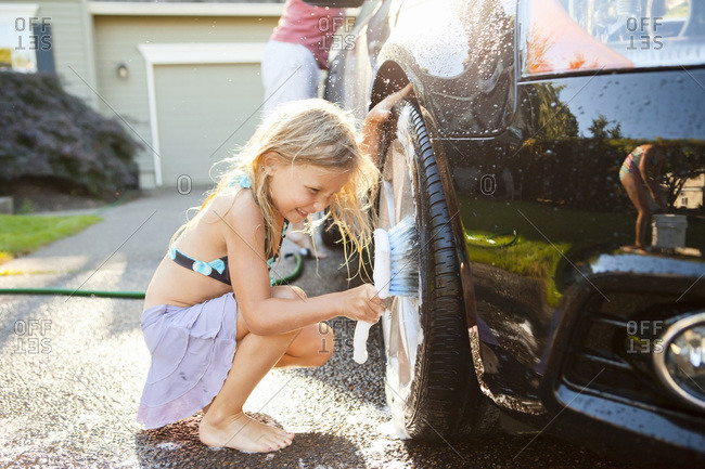 Young daughters help father wash their car in the driveway of their home on a sunny summer afternoon in Portland, Oregon, USA