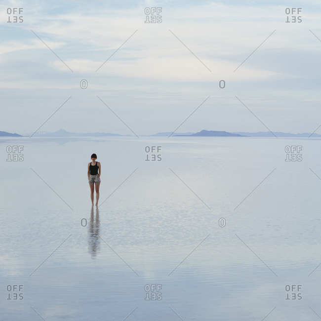 A woman standing on the flooded Bonneville Salt Flats, at dusk