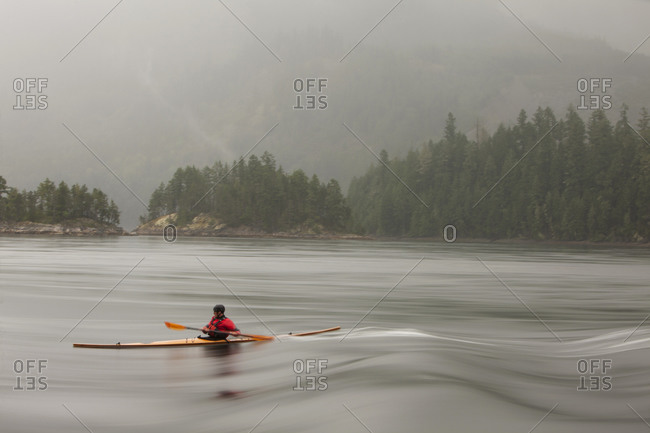 A man surfs the river in his cedar strip kayak