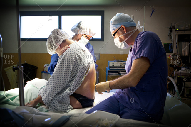 Doctor administering a spinal anesthesia into a woman prior to cesarean delivery