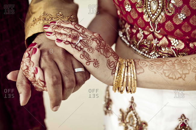 Mid-section view of Indian groom and bride holding hands