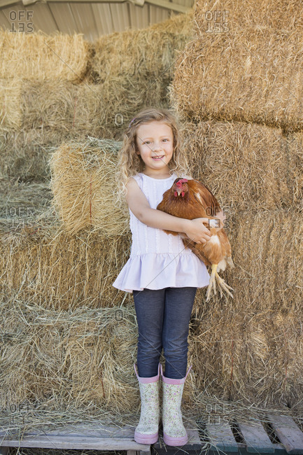 Pretty girl standing in hay barn and holding chicken in her arms