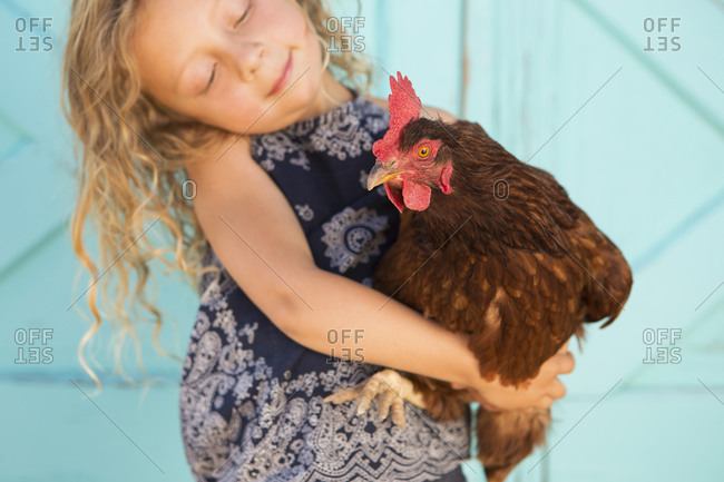 Cute girl holding a red chicken in her arms
