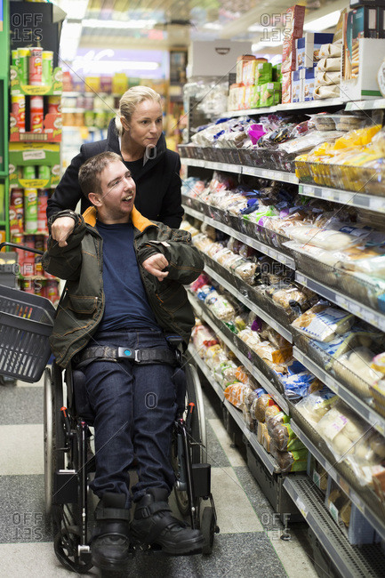Disabled man on wheelchair shopping with caretaker in supermarket