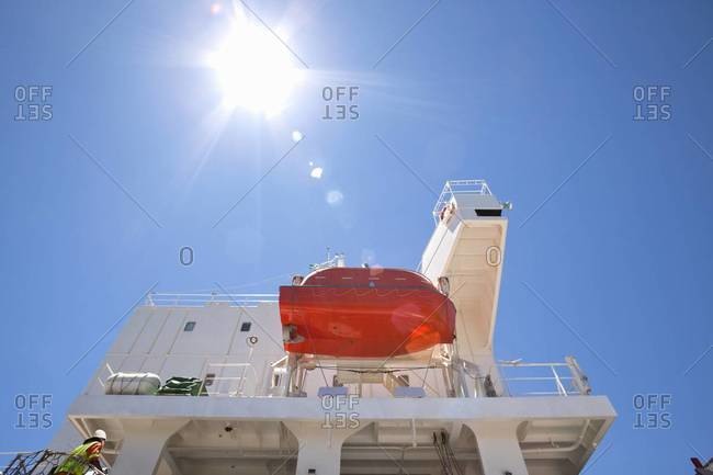 Sun shining above lifeboat hanging from container ship
