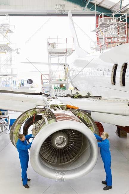 Engineers assembling engine on passenger jet in hangar