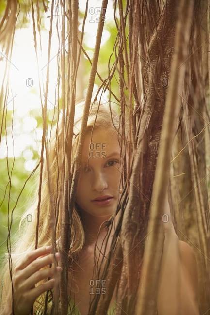 Caucasian woman peering through banyan tree vines