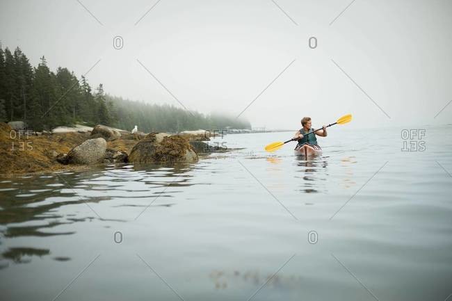 Man paddling a kayak on calm water in misty conditions. New York State, USA