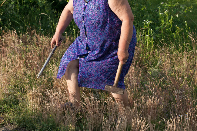 A woman in a purple dress carries a hammer and stake cross a field in rural Ukraine
