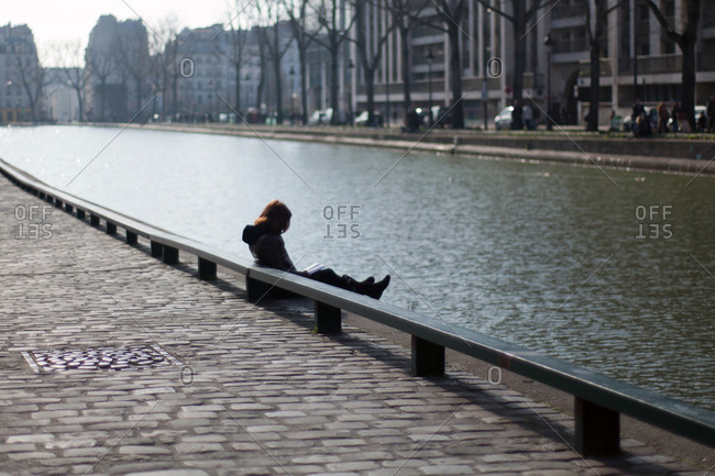 Woman sitting on the bank of Seine and reading book