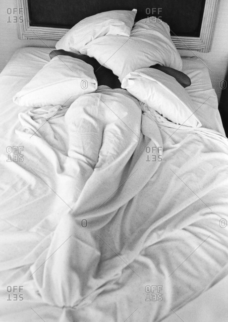 Back view of a person lying in bed, covered with pillows