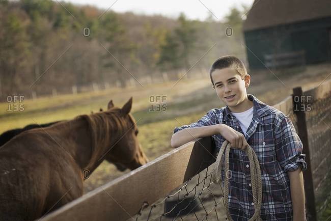 A boy standing by the fence of a horse paddock. A bay horse.