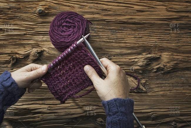 A woman holding two knitting needles, and a piece of knitting, in purple wool.