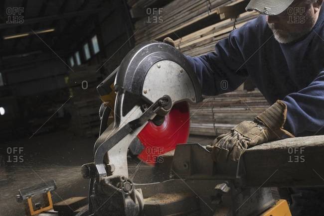 A man in protective eye goggles using a circular saw to cut timber.