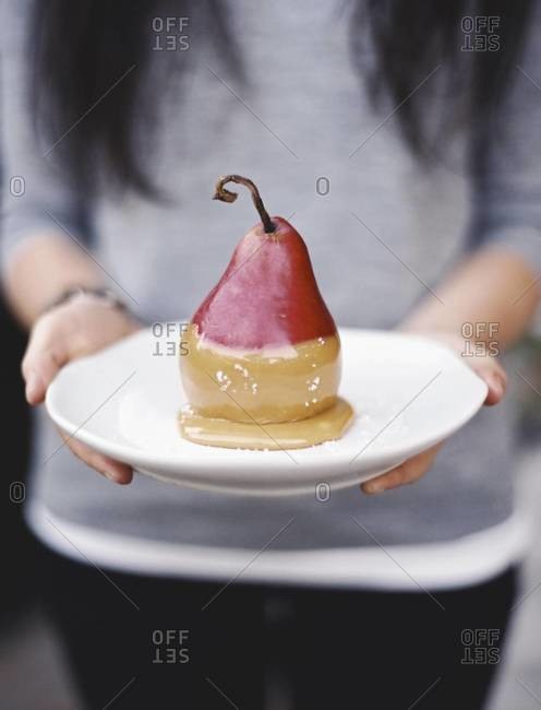 A woman holding a plate with a dessert of fresh pear dipped in fudge sauce.