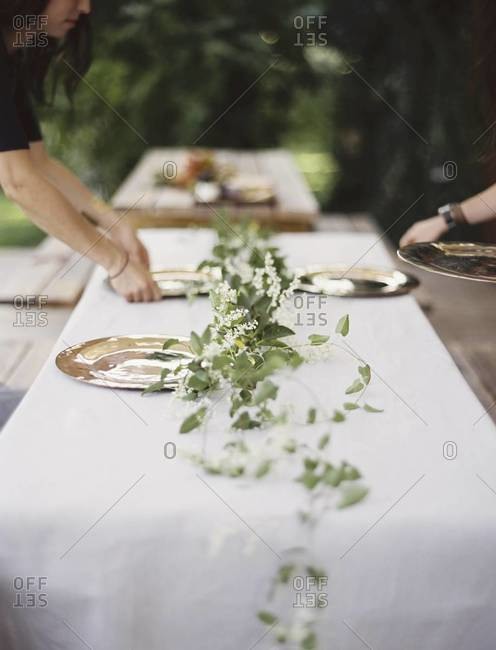 Two people leaning over a table laid outside with a white cloth and a central foliage table decoration