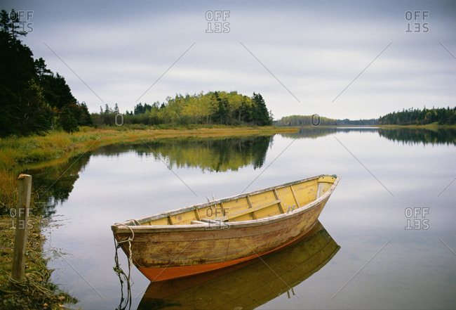 A small wooden dory or rowing boat moored on flat calm water