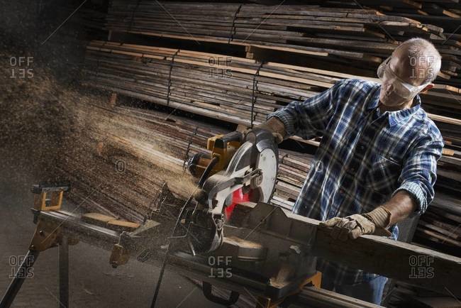 Man in protective eye goggles using a circular saw to cut timber
