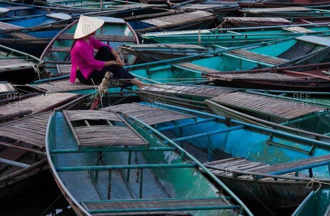 Lost in thought, a woman sits amidst a raft of boats Ninh Binh, Vietnam
