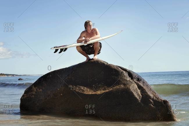 Surfer squatting on rock and waiting for waves