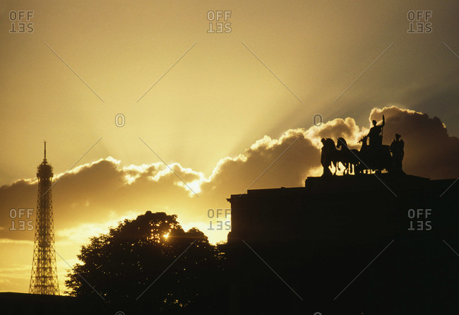 Sunset over Paris with the silhouette of Eiffel Tower and statue atop the Triumphal Arch of Carrousel in France