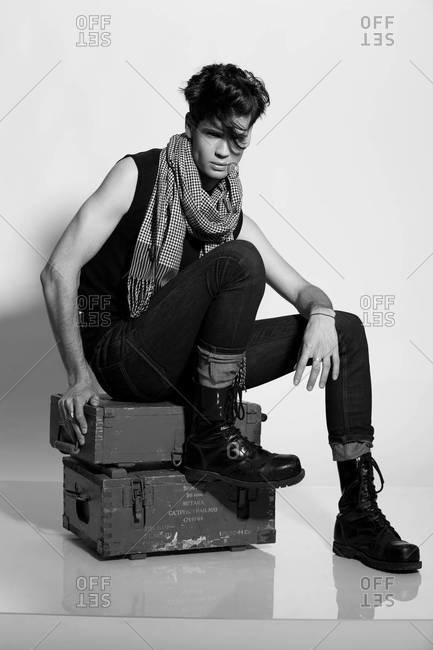 A black and white studio portrait of a stylish handsome man in black shirt and skinny black jeans with scarf, rockabilly style