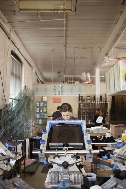Young woman printing t-shirts with manual screen printing carousel