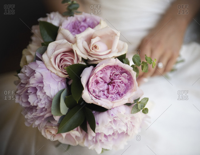 A bride holding a bridal bouquet of pastel colored pale pink roses and peonies.