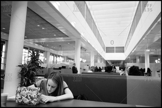Girl writing on desk while sitting in hall