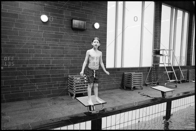 Boy standing on swim start in swimming pool ready to jump