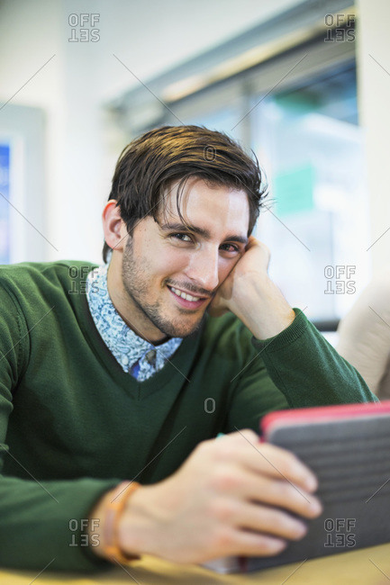 Portrait of university student with digital table sitting at table in common room