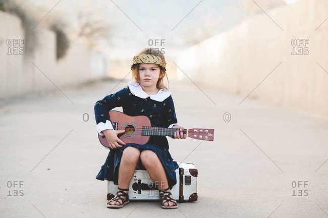 Young girl sitting on a case holding a guitar