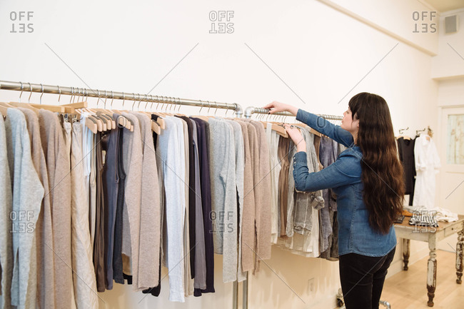 Female store assistant on rearranging clothing rail at clothing store