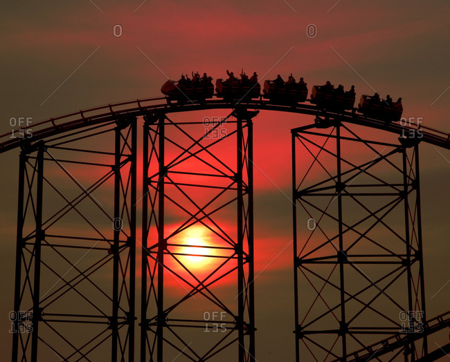 Silhouette of riding roller coaster under sunset