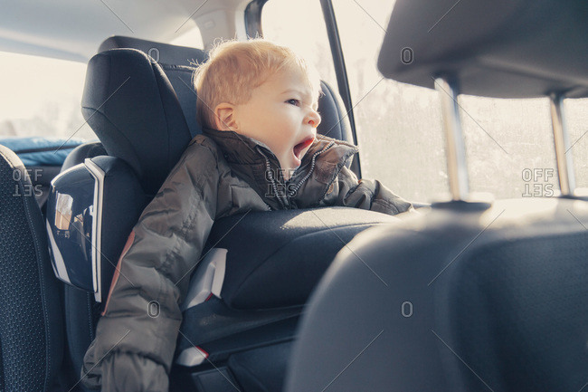 Little boy sitting in back-seat car seat, yawning
