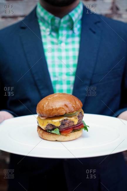 Mid section view of man holding hamburger on plate
