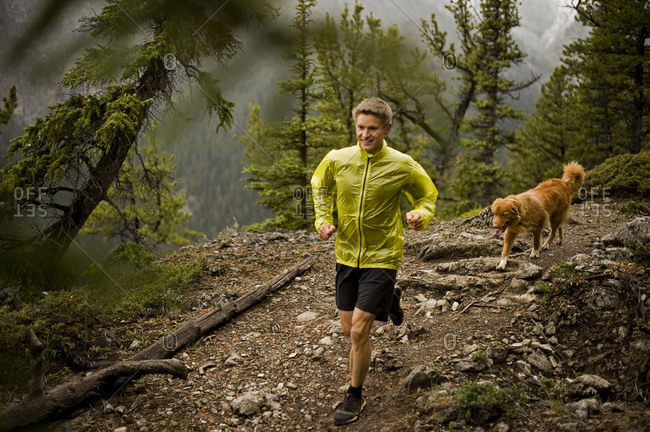 Athletic young man runs on a mountain trail with a happy dog