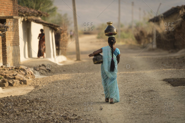 Woman walking with water jugs at a village in Central India